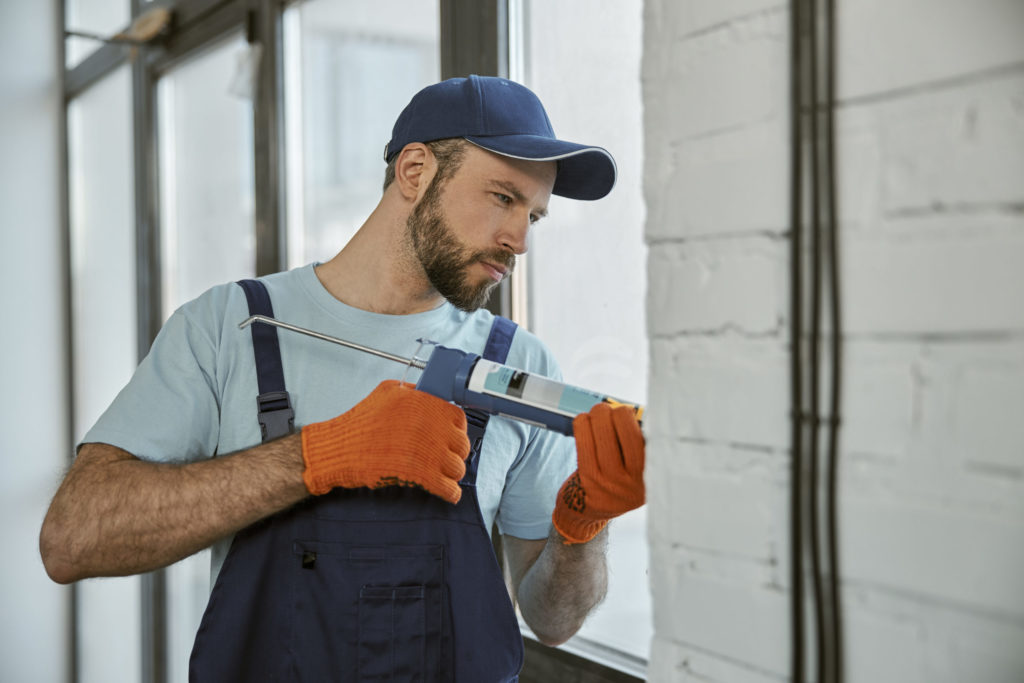 Bearded young man repairing window with special tool